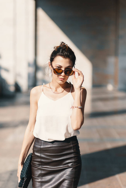 Refined business woman holding fashionable sunglasses down looking above them on blurred background - Photo, Image
