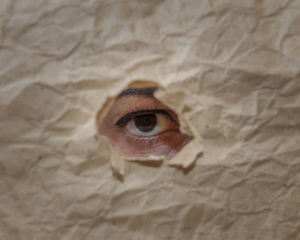 Око дівчини з макіяжем дивиться в розірваний отвір в папері
 - Фото, зображення
