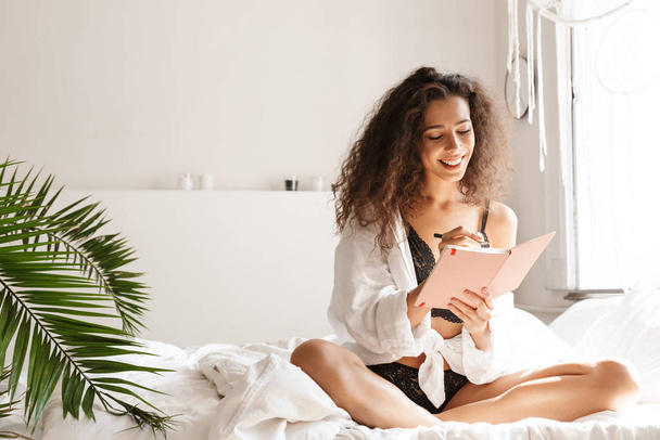 Image of woman wearing lingerie holding diary book on bed in apa - Φωτογραφία, εικόνα