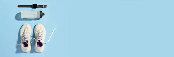 Фітнес-трекер, білі кросівки та пляшка води під ранковим сонячним світлом на синьому фоні. Ранковий біг. Прапор. Плоский прошарок, вид зверху
 - Фото, зображення