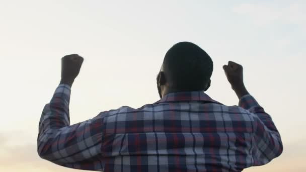 Black man rising hands up showing success gesture, winner, magic hour, back-view - Filmagem, Vídeo