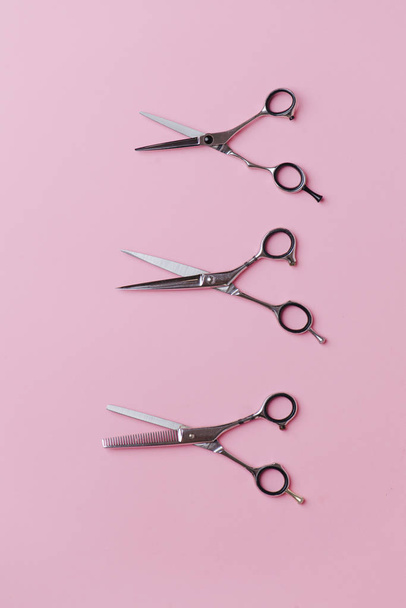 Three pairs of metal hairdresser scissors in a vertical row over pink background - Foto, Imagen