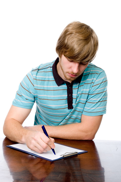 Серьезный молодой человек сидит за столом с ручкой в руке
. - Фото, изображение