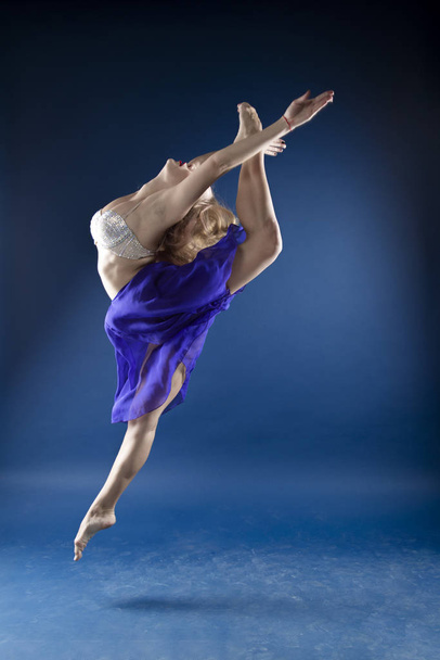 girl dancer in a jump and a beautiful pose on a blue background - Foto, Bild