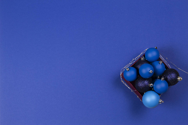 Blauwe kerstballen en slinger in de doos op blauwe achtergrond. Bovenaanzicht - Foto, afbeelding