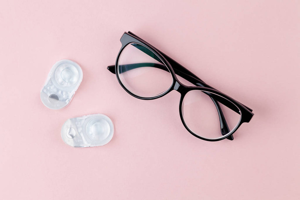 Glasses and contact lenses on pink background. Concept of vision correction. Top view, copy space. - 写真・画像