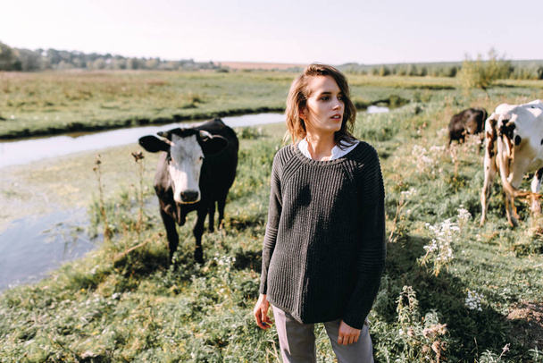 Γυναίκα σε πουλόβερ ποζάρουν στον τομέα με τις αγελάδες - Φωτογραφία, εικόνα