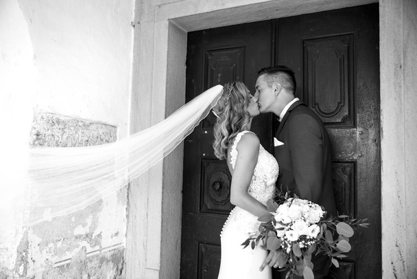 A csók. Menyasszony és a vőlegény csókokkal gyengéden előtt templom portál. - Fotó, kép