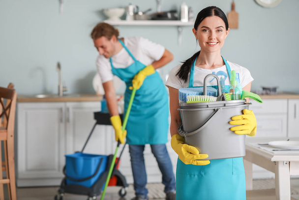 Vrouwelijke conciërge met schoonmaakmiddelen in de keuken - Foto, afbeelding