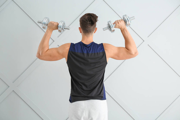 Sporty young man with dumbbells on light background - Photo, Image