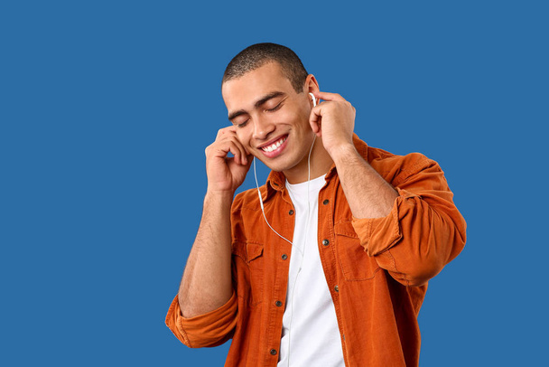 Portrait of handsome young man listening to music on color background - Foto, afbeelding
