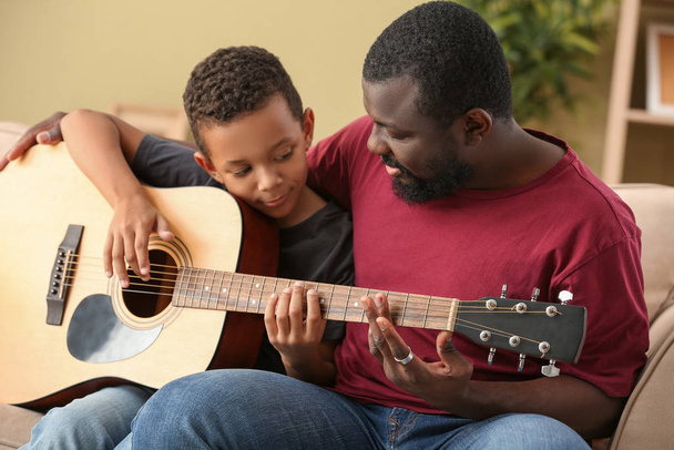 Uomo afro-americano che insegna al suo piccolo figlio a suonare la chitarra a casa - Foto, immagini