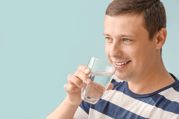 Portrét pohledného muže pití sladké vody na barevném pozadí - Fotografie, Obrázek