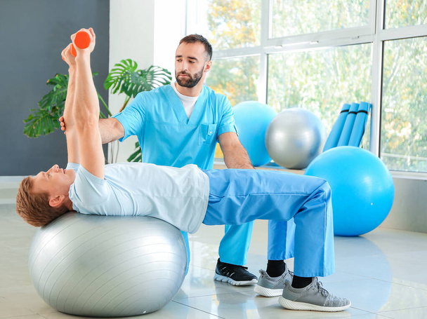 Fysiotherapeut werkt met mannelijke patiënt in revalidatiecentrum - Foto, afbeelding