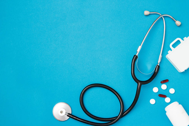 Stethoskop mit Pillen auf blauem Hintergrund. Gesundheitskonzept. Draufsicht, flache Lage, Kopierraum. - Foto, Bild
