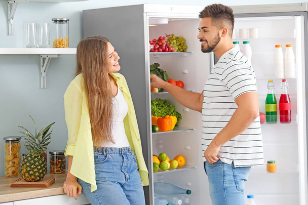 Young couple taking food out of fridge in kitchen - Photo, Image