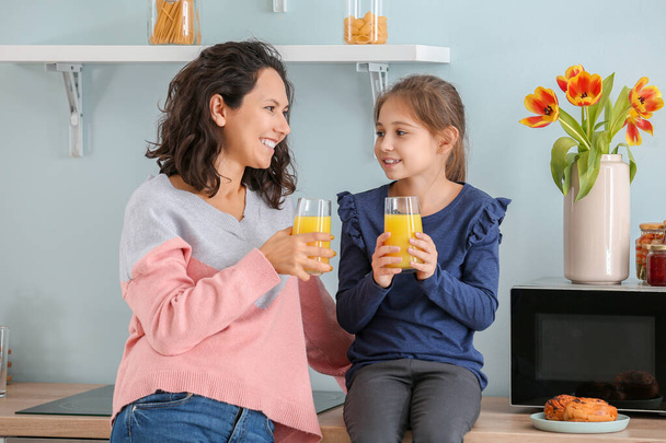 Menina com a mãe bebendo suco na cozinha
 - Foto, Imagem