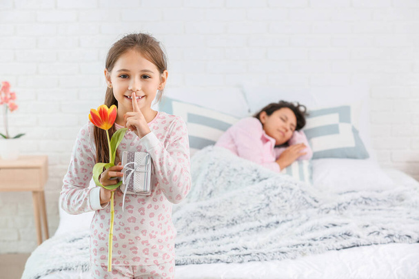 Kleines Mädchen mit Geschenk für Mutter zeigt Schweigegegeste im Schlafzimmer - Foto, Bild