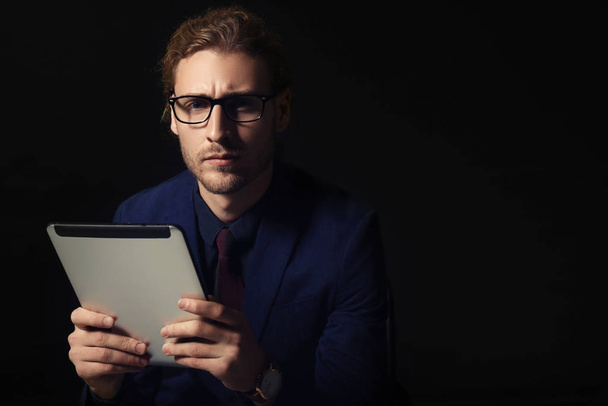 Portrait of handsome businessman with tablet computer on dark background - Photo, Image