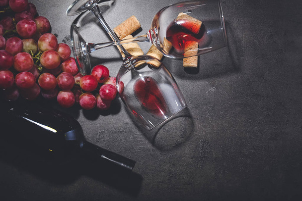 Μπουκάλι κρασί με σταφύλια, ποτήρια και φελλούς σε σκούρο φόντο - Φωτογραφία, εικόνα