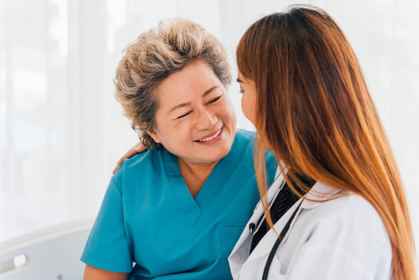 Giovani 30 anni medico asiatico conforta e consola una felice sorridente donna asiatica anziana con i capelli grigi che indossa un abbigliamento paziente in ospedale
 - Foto, immagini