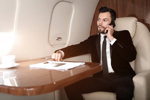 Επιχειρηματίας μιλάει τηλεφωνικά στο σύγχρονο ιδιωτικό αεροπλάνο - Φωτογραφία, εικόνα