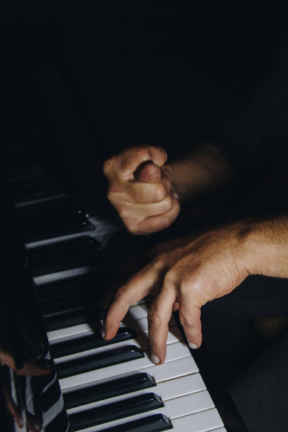 two male hands on the piano. palms lie on the keys and play the keyboard instrument in the music school. student learns to play. hands pianist. black dark background. - Foto, immagini