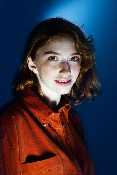 Portrait of redhead girl with freckles closeup on classic blue background. - Фото, зображення