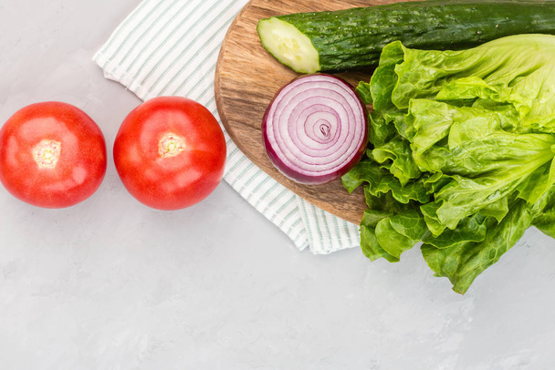 Healthy vegetarian dish on table, vegetable salad with fresh tomato, cucumber, lettuce, red onion on gray concrete background. Diet menu. Top view. Flat lay, mockup, template with copy space - 写真・画像