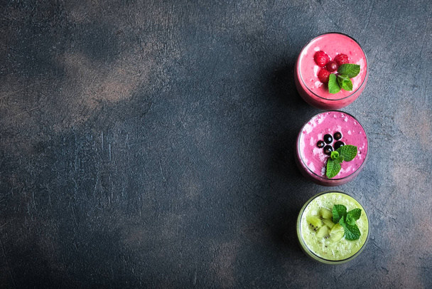Colorful smoothie, fresh vitamins drink with raspberry, kiwi, banana and blueberries. Healthy detox vitamin diet or vegan food concept on a dark background, top view with copy space. - 写真・画像