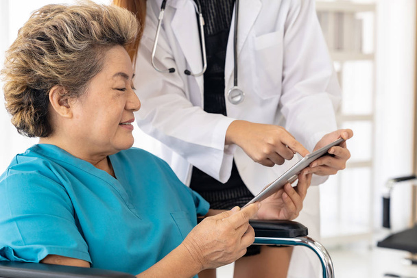 Azji zaufanie lekarz za pomocą cyfrowej tabletki wyrażając obawy zdrowotne ze starą starszą panią pacjent siedzieć na wózku inwalidzkim - Zdjęcie, obraz