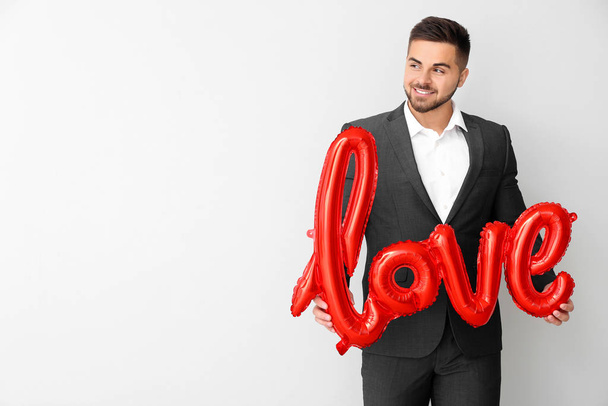 Handsome man with balloon in shape of word LOVE on light background. Valentine's Day celebration - Zdjęcie, obraz