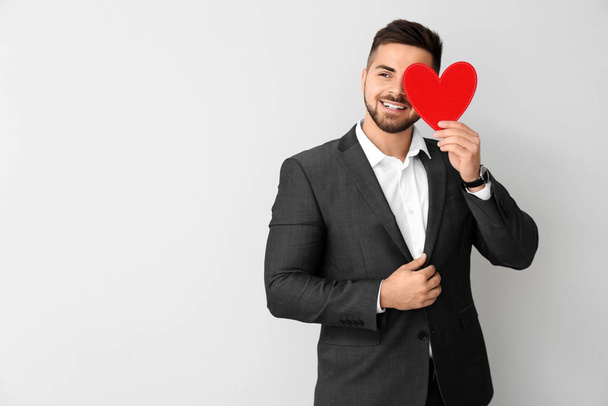Handsome man with red heart on light background. Valentine's Day celebration - Foto, immagini