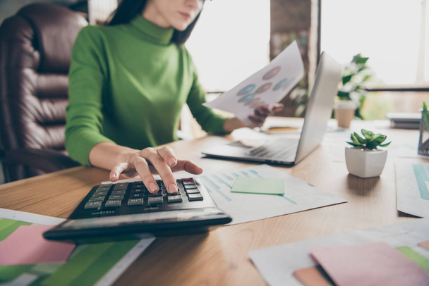 Cropped closeup photo of busy business lady notebook table hold paper stats calculating numbers sums money income sit chair wear green turtleneck modern office - Foto, afbeelding