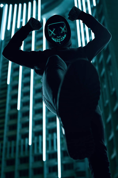 Homem anônimo de capuz preto escondendo seu rosto atrás de uma máscara de néon
 - Foto, Imagem