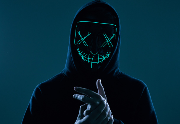 Анонімний чоловік в чорному светрі ховає обличчя за неоновою маскою
 - Фото, зображення