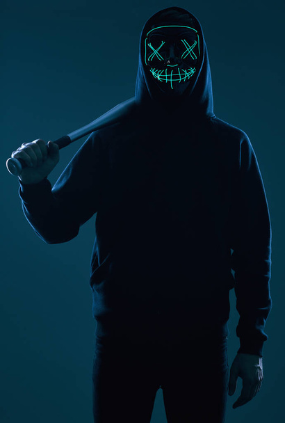 Uomo criminale anonimo con mazza da baseball con cappuccio nero e maschera al neon
 - Foto, immagini
