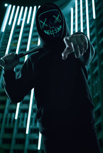 Hombre criminal anónimo con bate de béisbol con capucha negra y máscara de neón
 - Foto, imagen