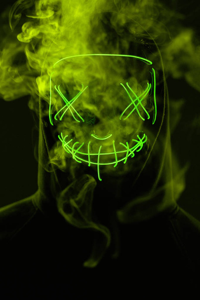 Ανώνυμος άνθρωπος κρύβει το πρόσωπό του πίσω από μάσκα νέον σε ένα έγχρωμο καπνό - Φωτογραφία, εικόνα