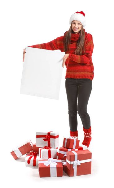 Beautiful young woman with Christmas gifts and blank poster on white background - Photo, image