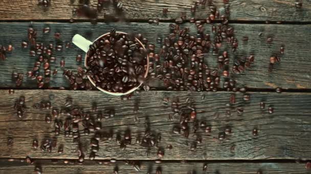 Arabica kávová zrna spadají do průhledného hrnku na dřevěné podlaze. - Záběry, video