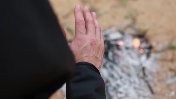 Egy fekete köpenyes szerzetes csuklyában ül egy üres telken, és felmelegszik a tűz mellett. - Felvétel, videó