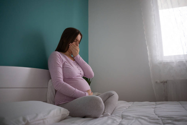 妊娠中の女性はベッドに座って吐き気を催している - 写真・画像