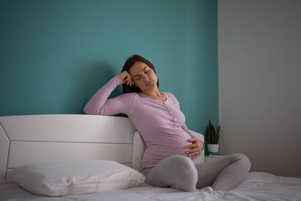 Zwangere vrouw zit in bed en voelt zich niet goed. - Foto, afbeelding