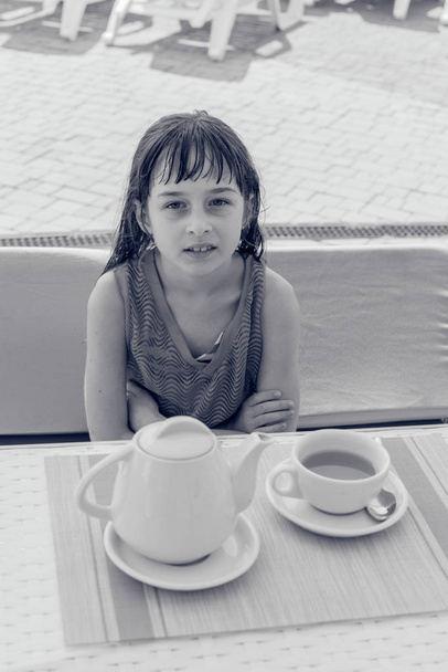 Una bambina di 9 anni beve tè nero in un parco acquatico o in vacanza a bordo piscina.Foto in bianco e nero
 - Foto, immagini