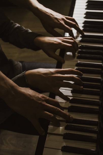 playing four male hands on the piano. palms lie on the keys and play the keyboard instrument in a music school. student learns to play. hands of a pianist. black dark background. - 写真・画像