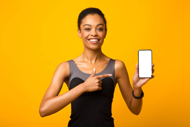 Афроамериканська дівчинка, яка демонструє смартфон, позиціонує пальця, жовте тло - Фото, зображення