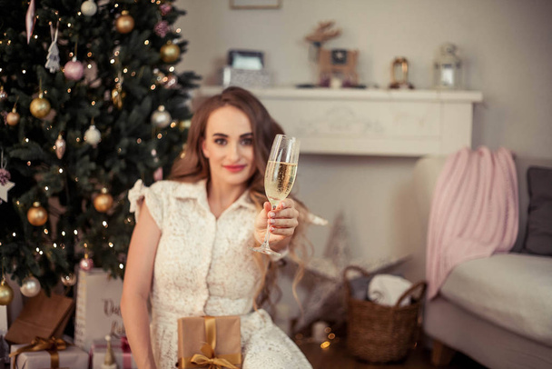 Красива молода жінка сидить на ялинці і відкриває подарунки. Різдво. Новий рік. Затишний
. - Фото, зображення