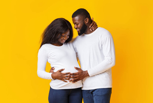 Embarazada pareja enamorada abrazando y hablando sobre fondo amarillo
 - Foto, Imagen