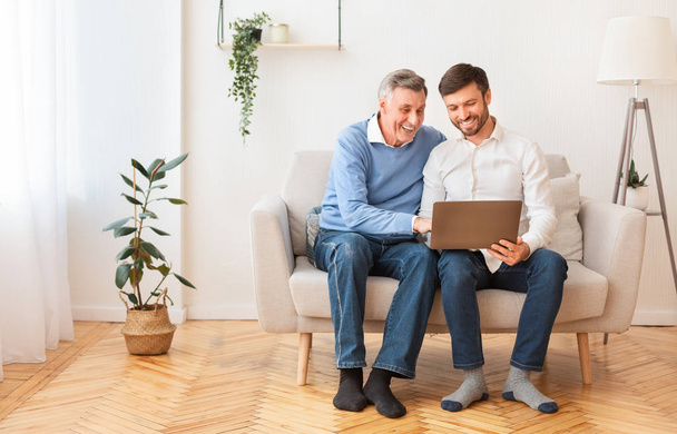 Adult Son Teaching Senior Father To Use Laptop Sitting Indoor - Photo, Image